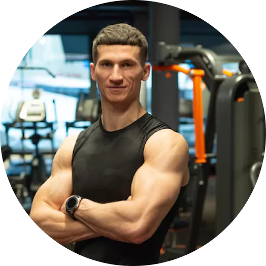 A man in a gym, wearing a sleeveless black shirt, standing with arms crossed.